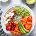 white bowl filled with rice bowl ingredients with a side of ranch and halved avocado.