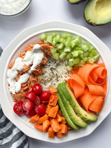 buffalo chicken rice bowls with a small bowl of ranch and an avocado cut in half.