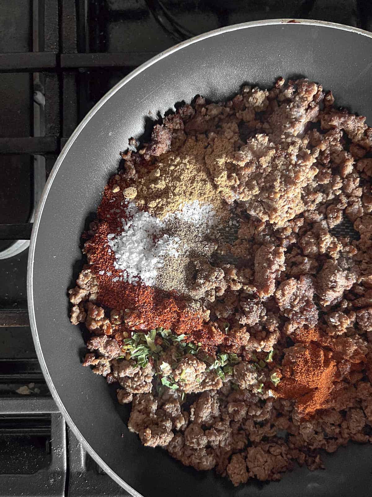 cooked ground beef with spices sprinkled on in a skillet.