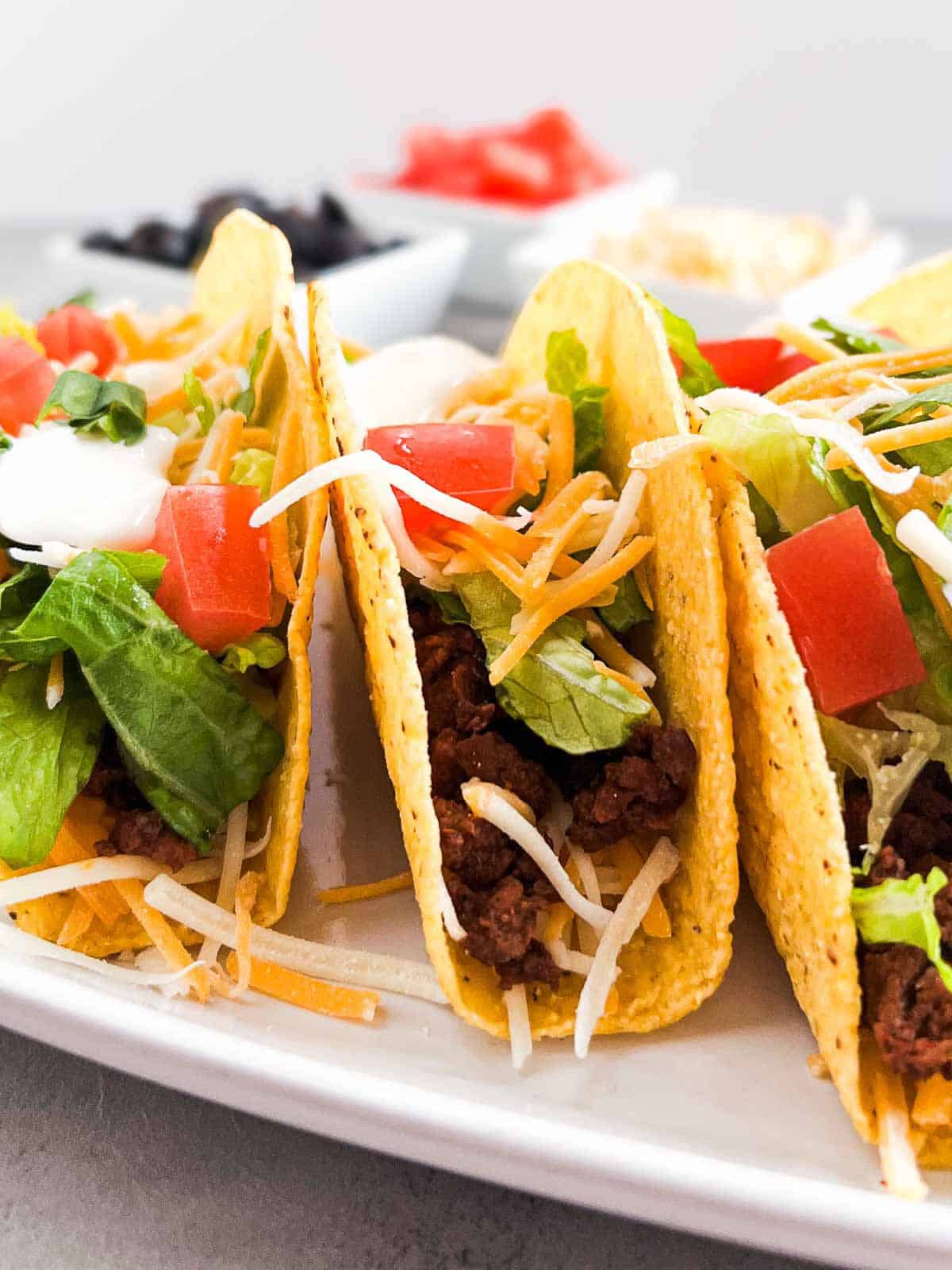 three hard shell tacos filled with ground beef, lettuce, cheese and tomatoes.
