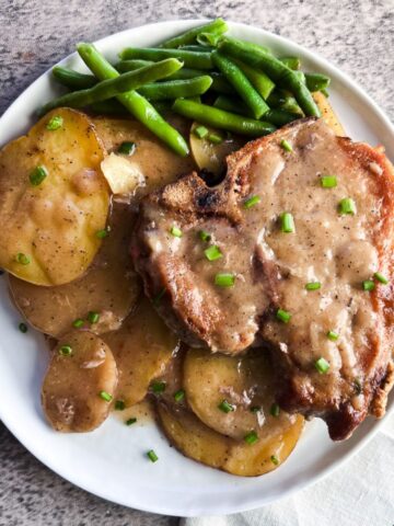 white plate full of pork chops, potatoes, and green beans.