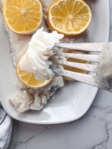 piece of cod on a fork above a platter of two pieces of cod.