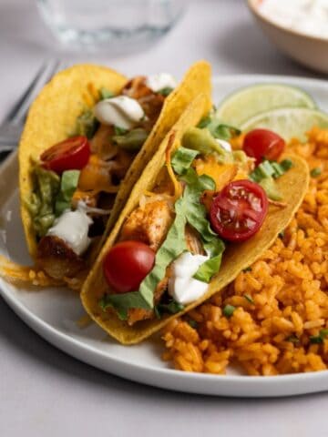 plate with two bags of chicken tacos with a side of Mexican rice.