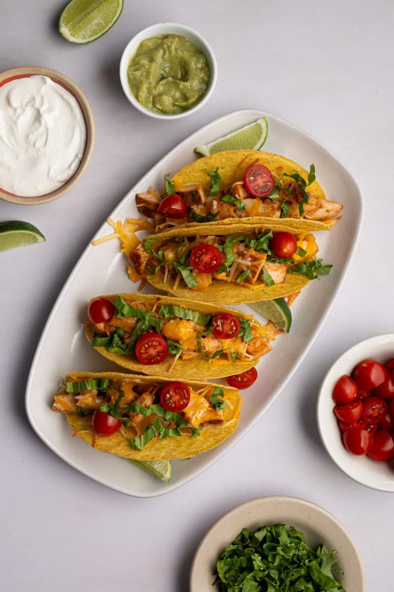 white platter of baked chicken tacos topped with letuce, and tomatoes. 