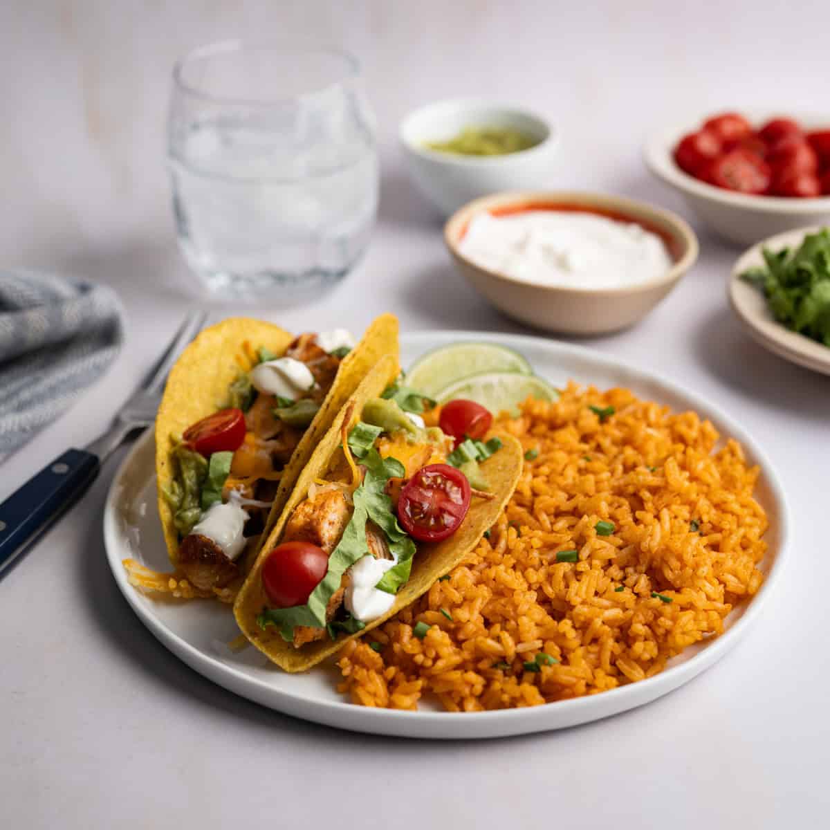 two chicken tacos with a side of mexican rice with bowls of toppings.