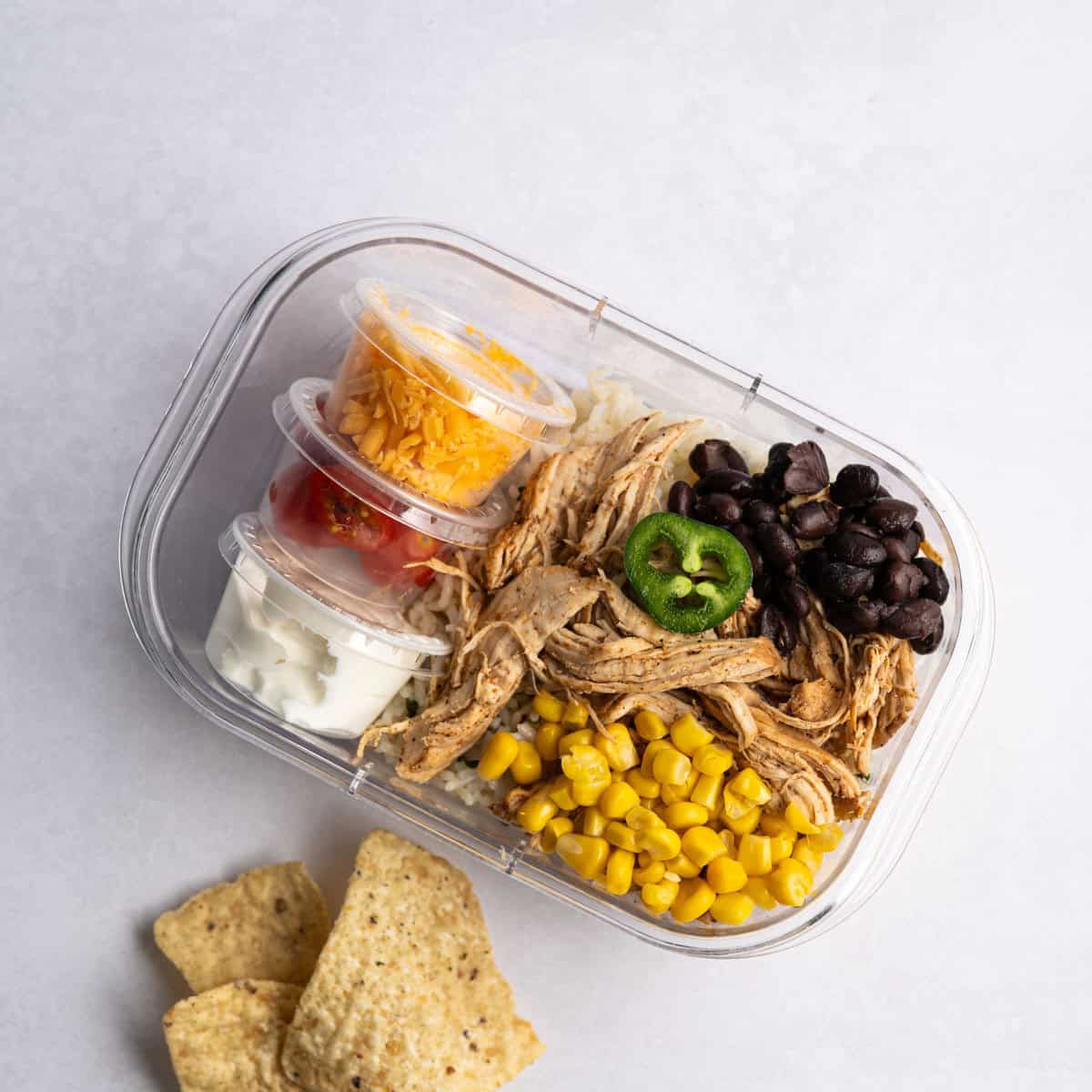 meal prep chipotle chicken container with a handful of tortilla chips.