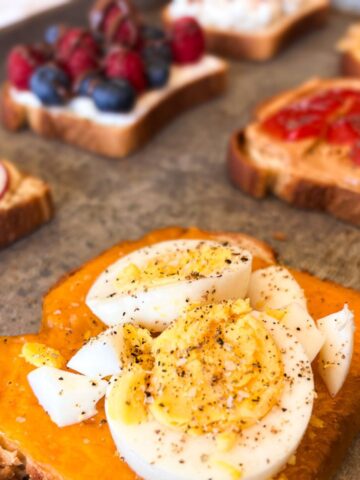 six slices of toast on a baking sheet with various toppings.