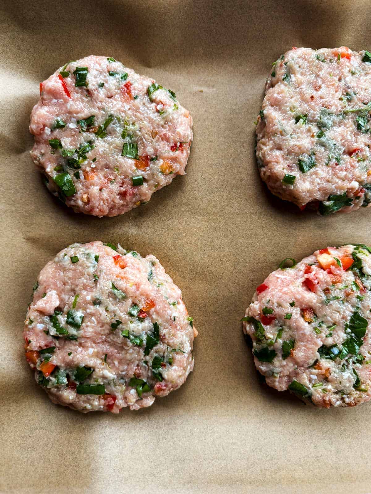 four uncooked chicken patties on a parchment covered baking sheet.