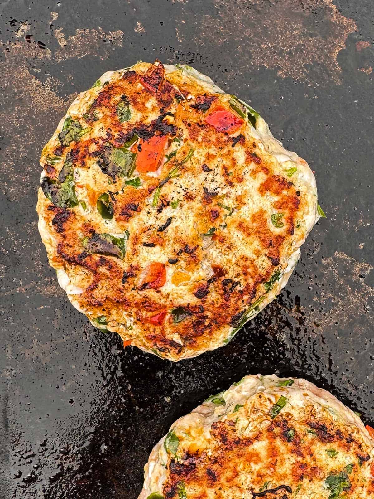 two chicken burger patties cooking on a blackstone.