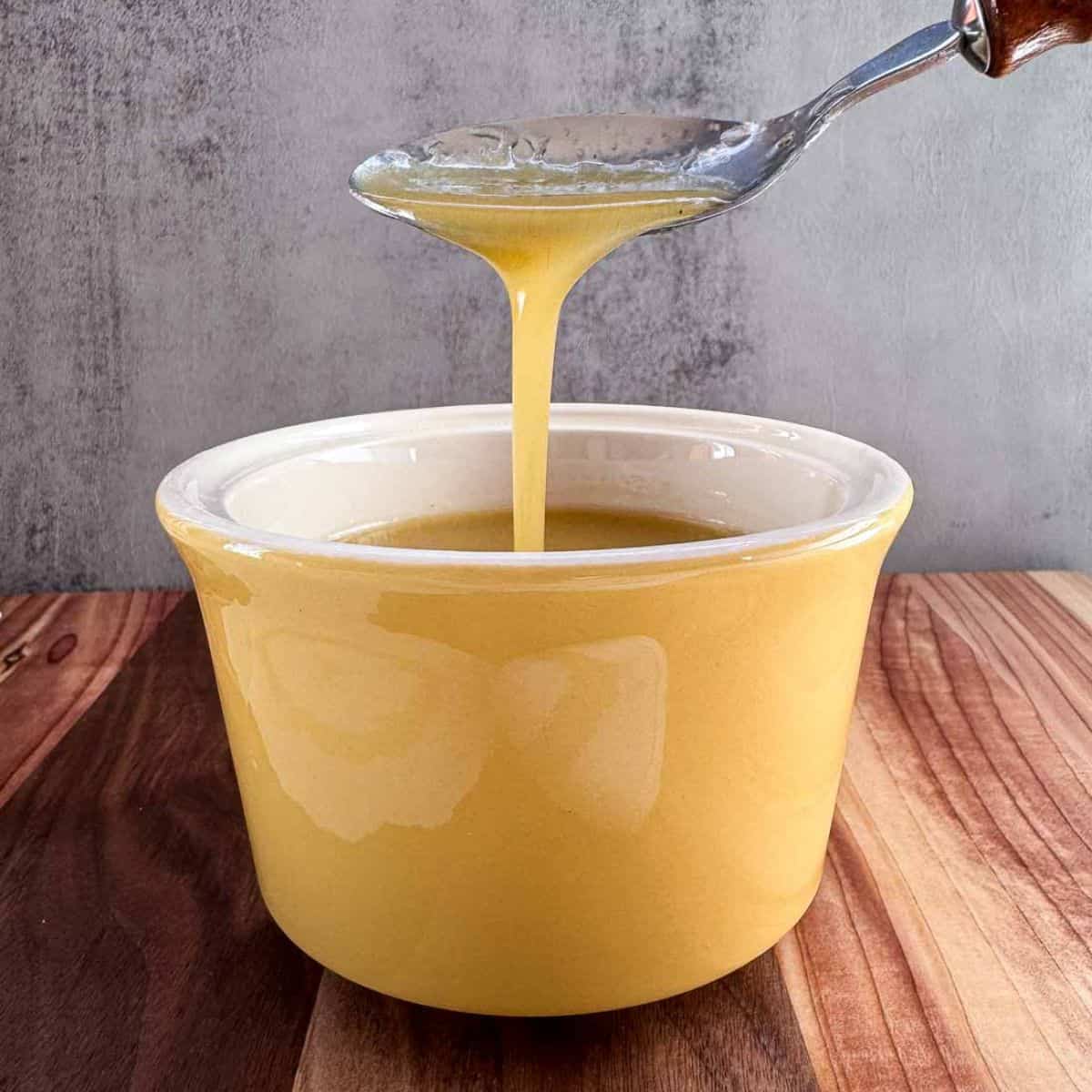 yellow dish with maple dijon dressing with a spoon drizzling it into it.