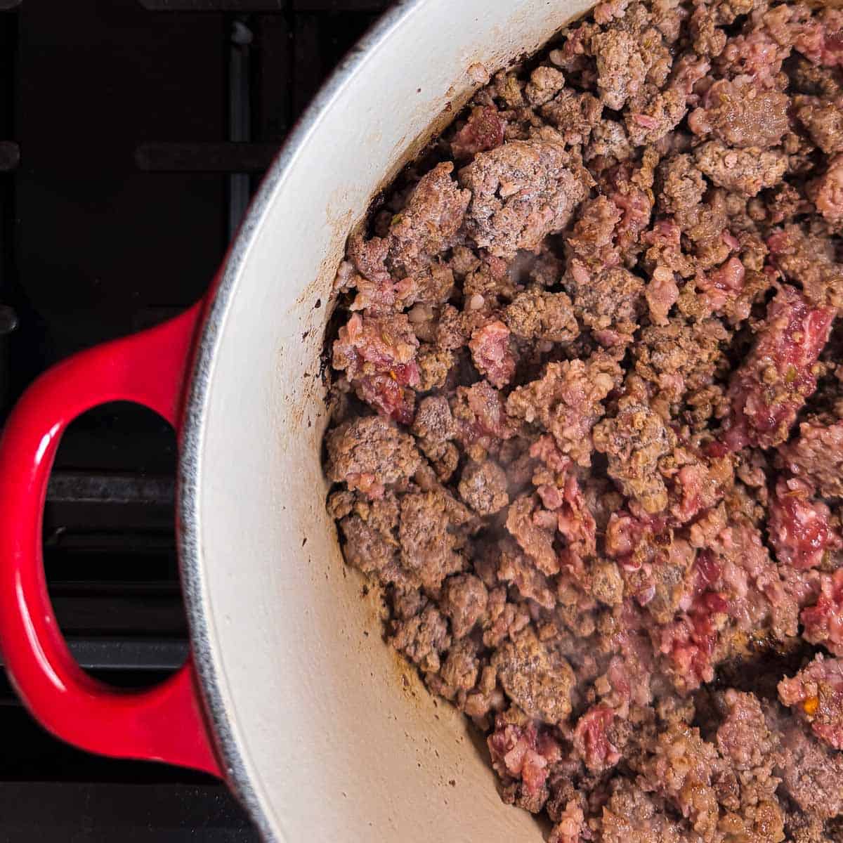 ground beef and Italian sausage cooked in a red dutch oven.