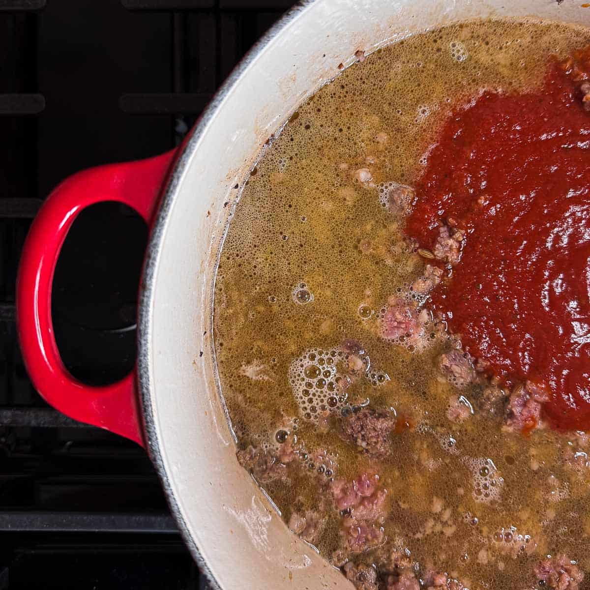 to the red dutch oven added the chicken broth and spaghetti sauce.