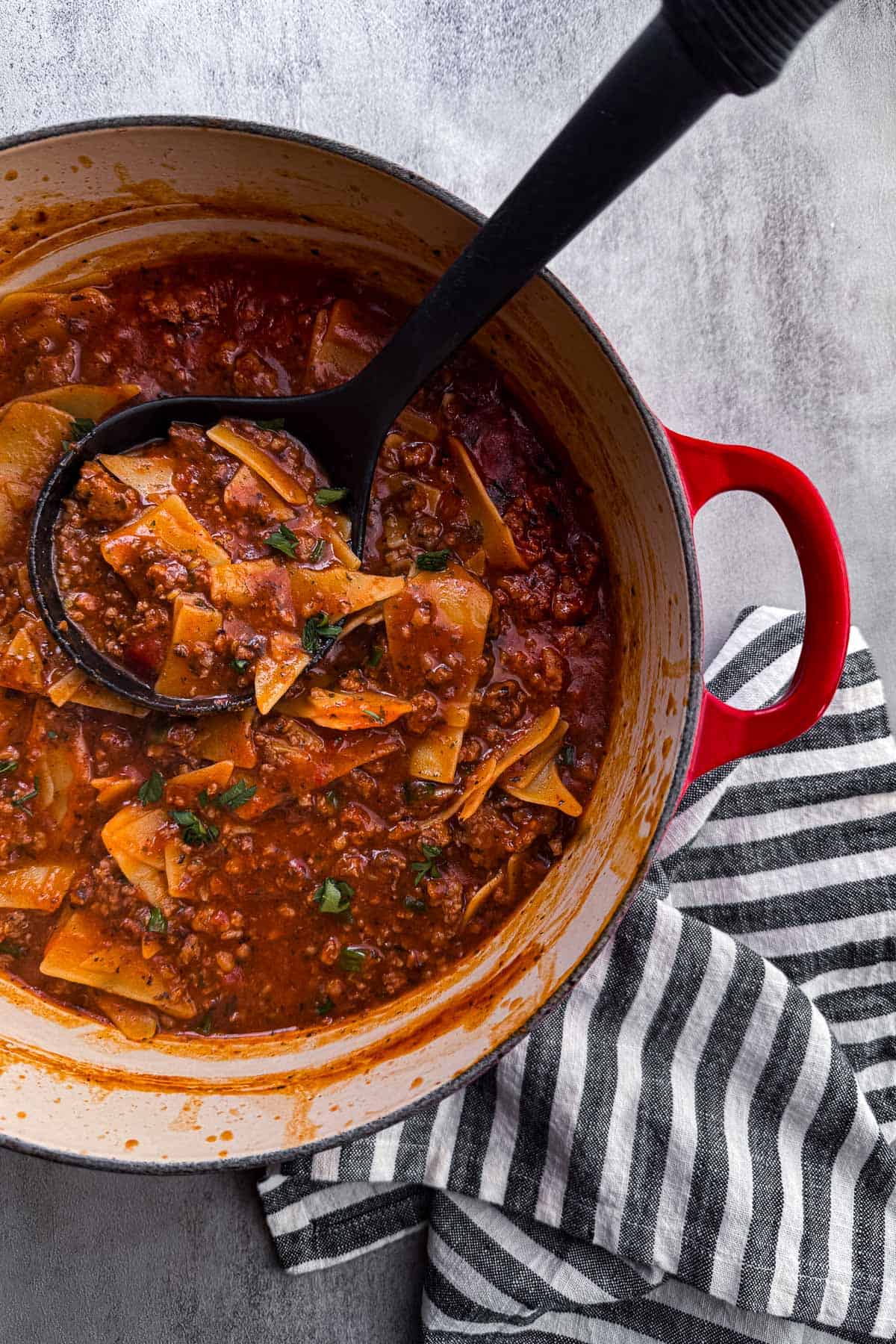 red dutch oven with cooked lasagna soup with a ladle.