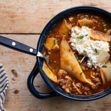 bowl of lasagna soup topped with cheese mixture, green onions and a spoon.