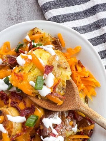 platter of smashed potatoes with a wooden spoon.