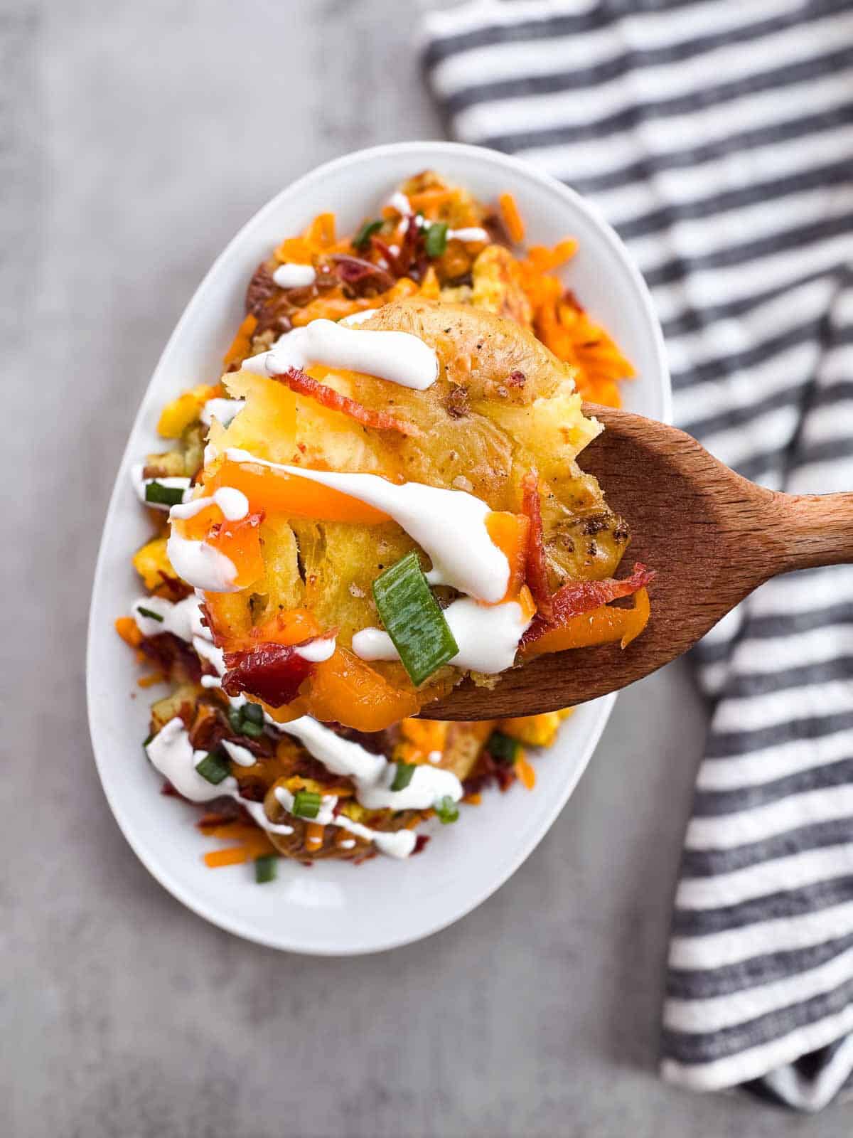 wooden spoon of smashed potatoes above a platter full.