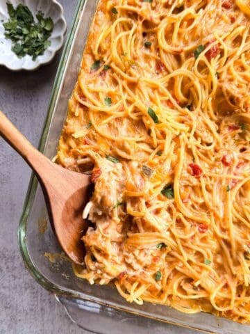 baking dish of chicken spaghetti with a wooden spoon and a small dish of chopped cilantro.