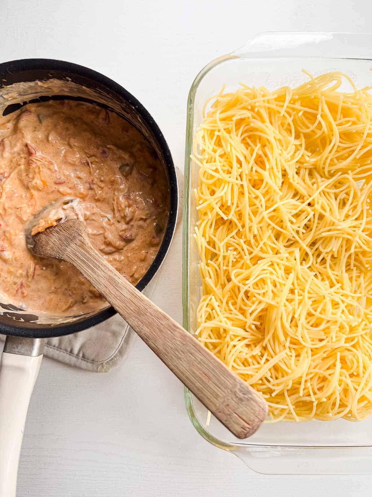 baking dish with cooked spaghetti noodles alongside a saucepan of cheesy sauce. 