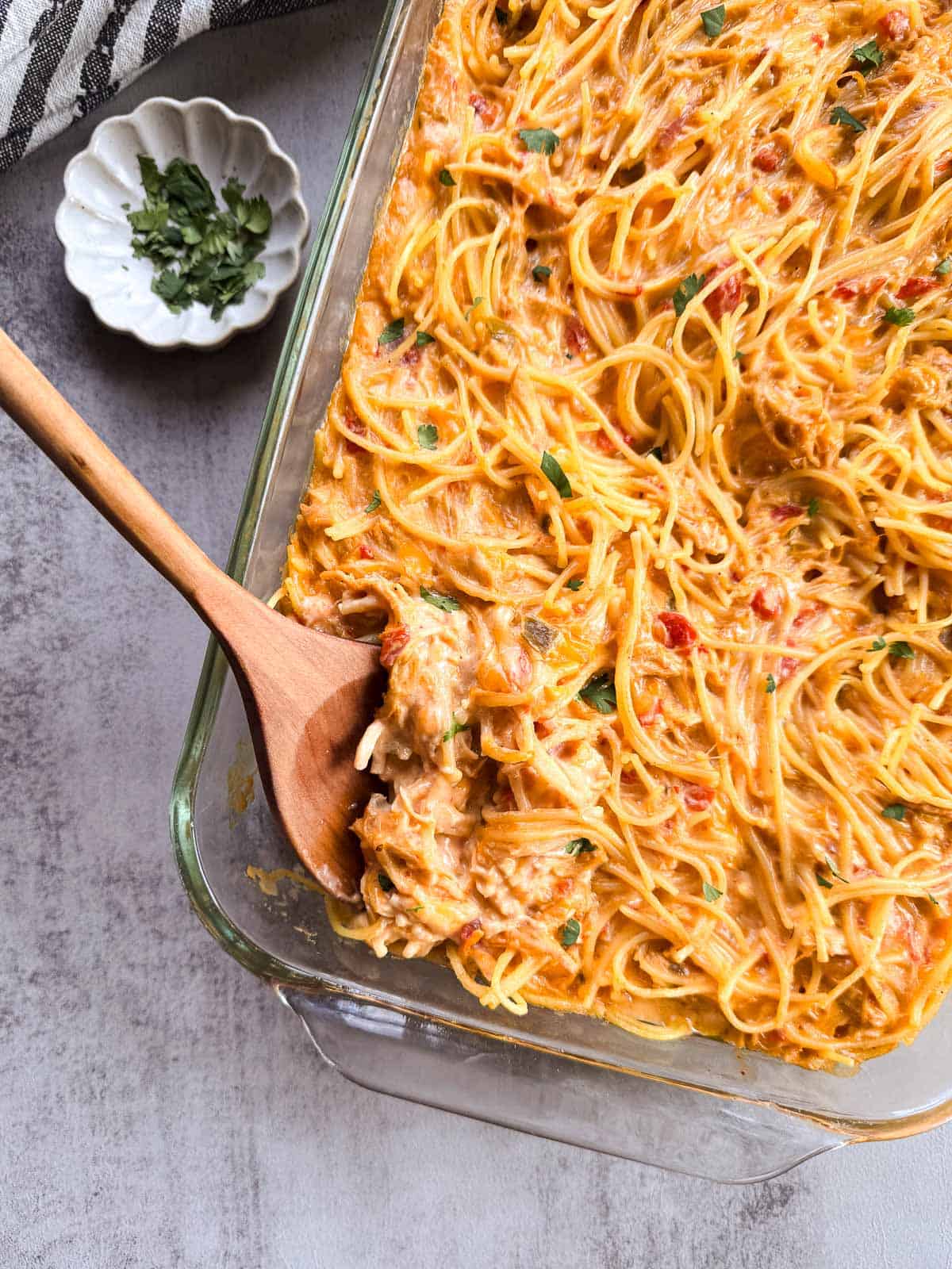 in a 9x13 inch baking dish with a wooden spoon alongside a small dish of chopped cilantro. 