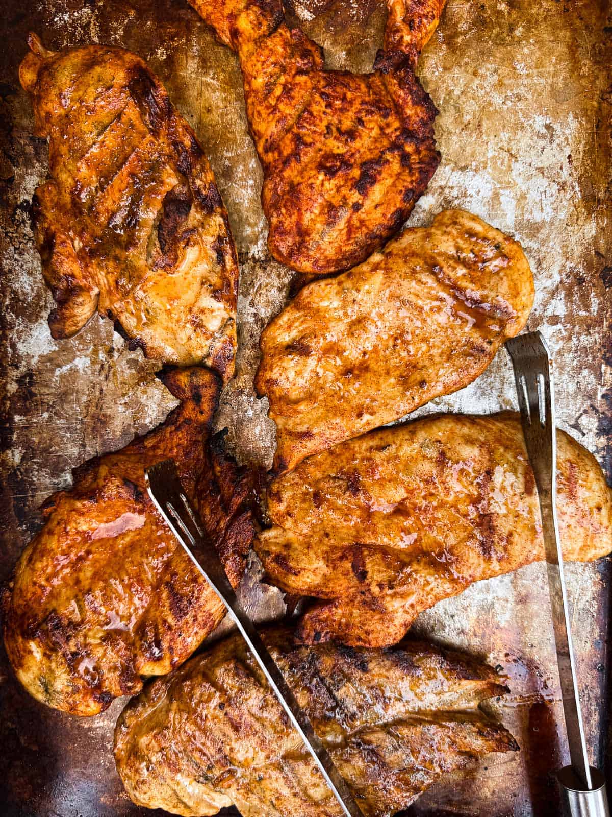 grilled chicken breasts on a baking sheet with tongs.