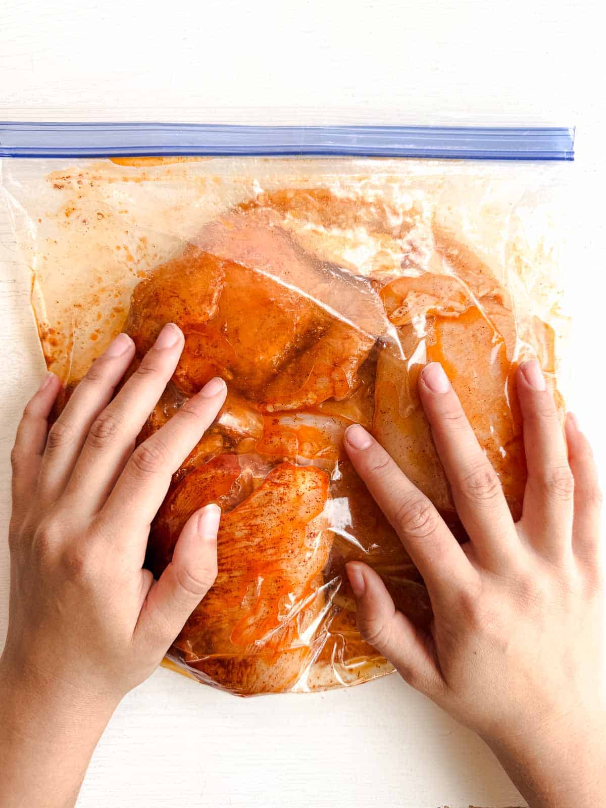 two hand coating the chicken in a marinade in a plastic bag.