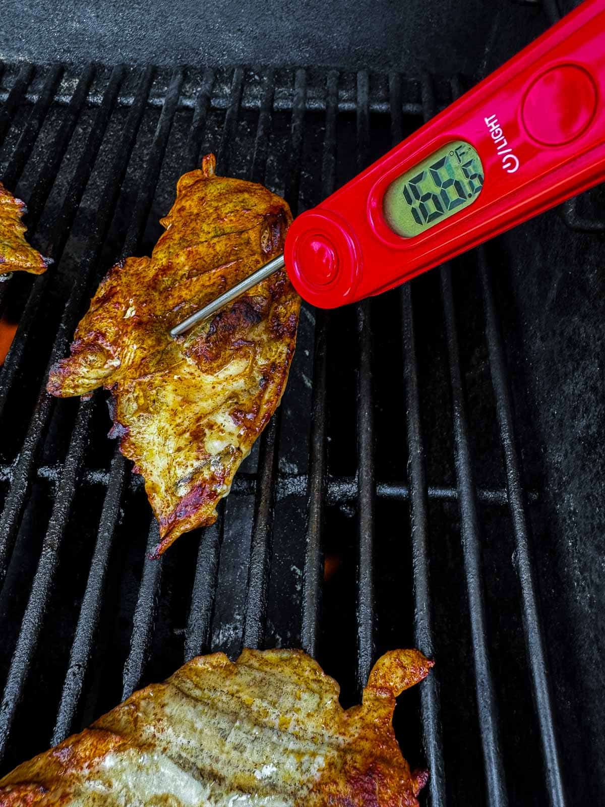 grilled chicken on a grill grate with a digital thermometer reading 166 degree F.