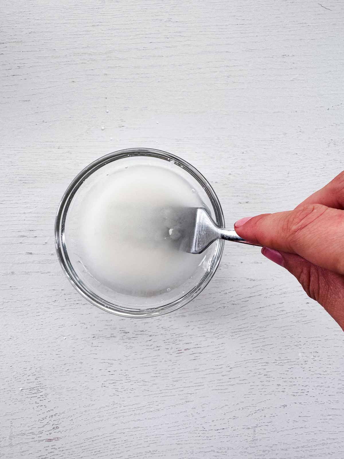 small glass bowl with water and cornstarch mixing with fork.