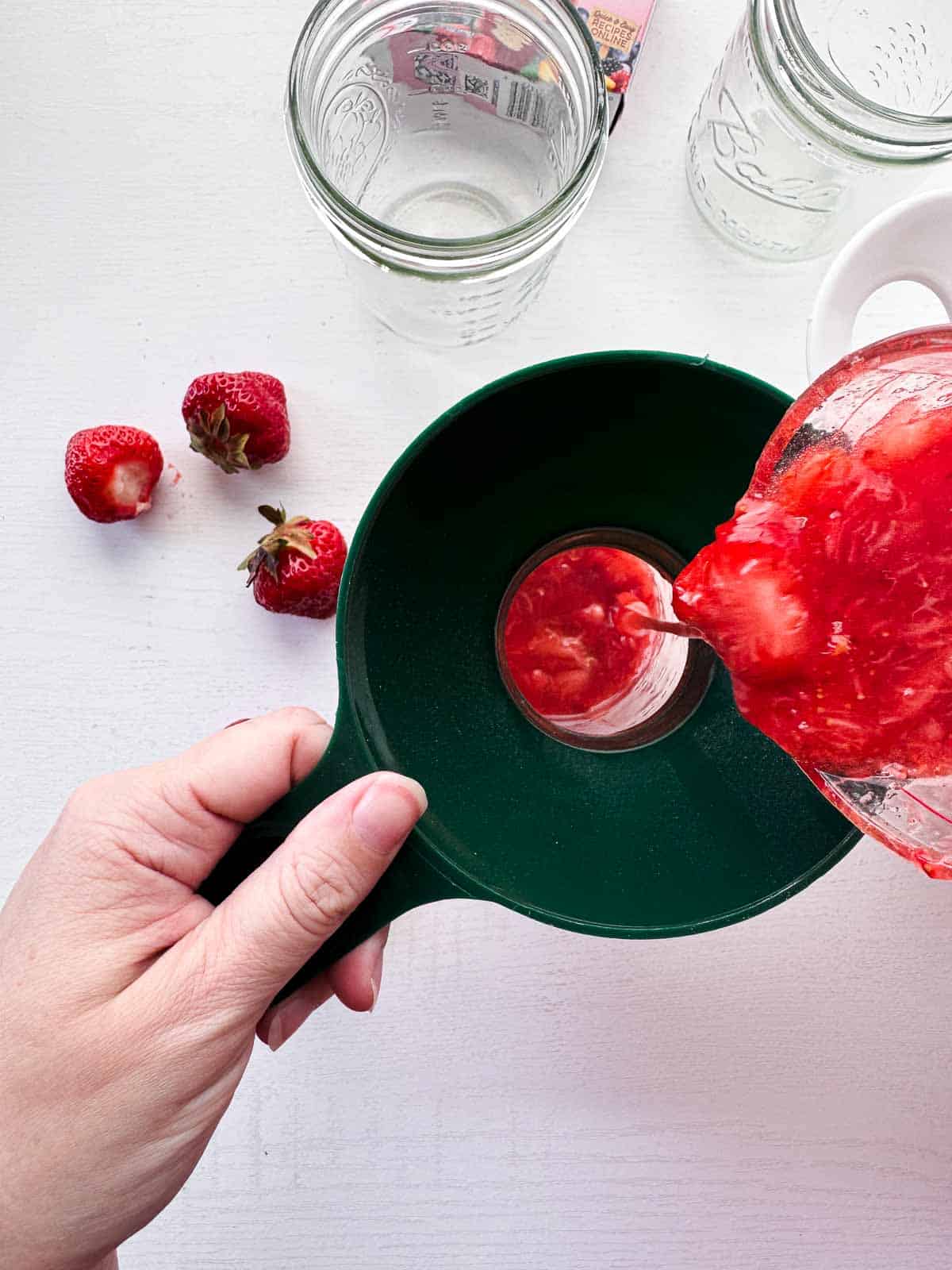 pouring jam into wide mouth funnel with a mason jar below.