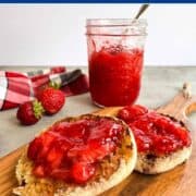 english muffin split, toasted and topped with strawberry jam on a wooden cutting board with a jar of jam in the background.