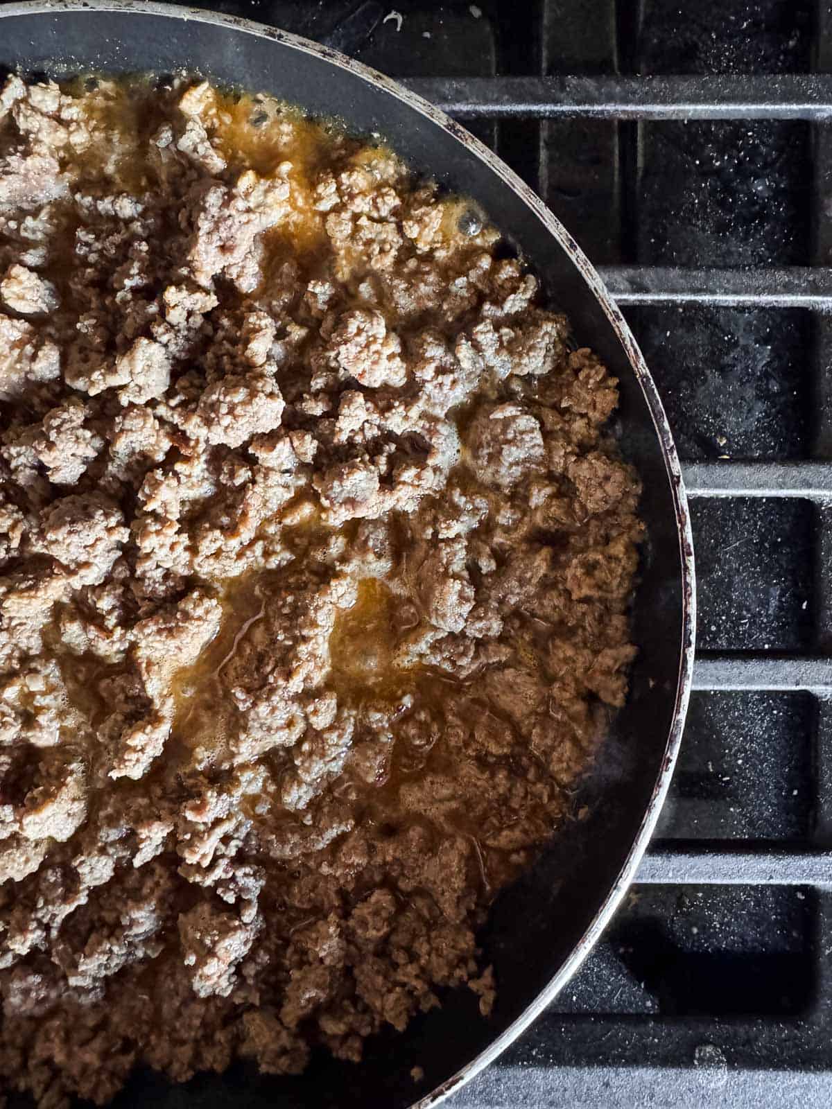 skillet on a stove top with cooked ground beef seasoned with taco seasoning. 