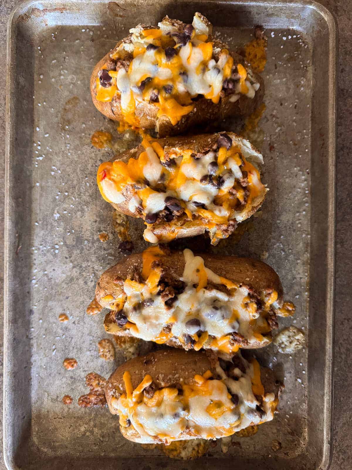 four baked potatoes stuffed with queso, black beans, taco meat and shredded cheese.