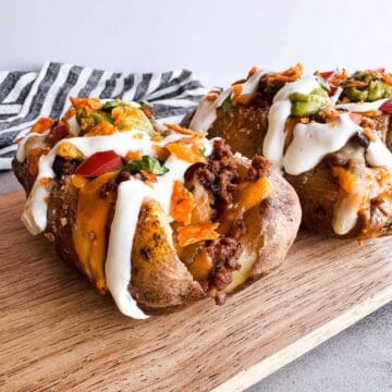 two taco baked potatoes topped with taco fillings on a wooden board.