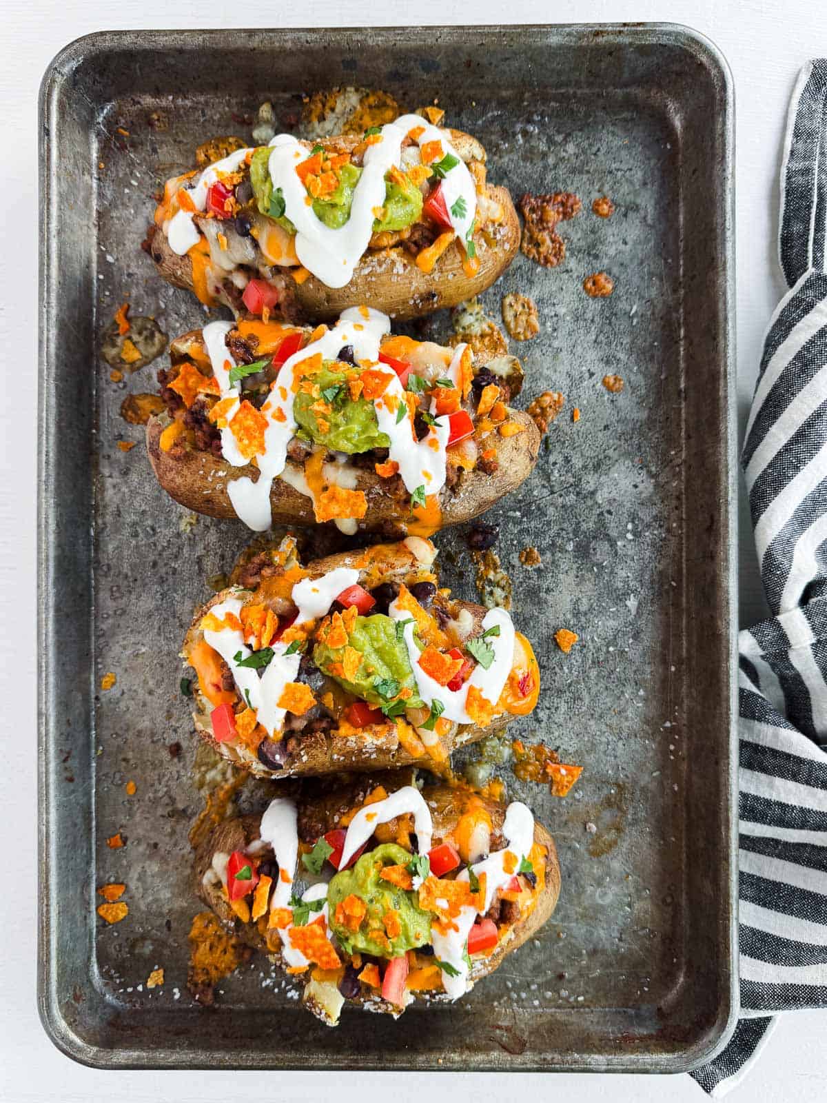 four taco baked potatoes on a baking sheet with all the toppings. 