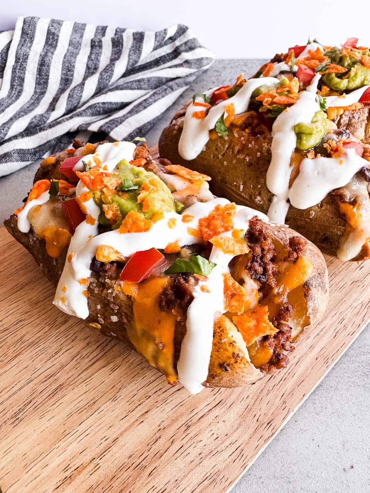three baked potatoes topped with taco toppings on a wooden board.