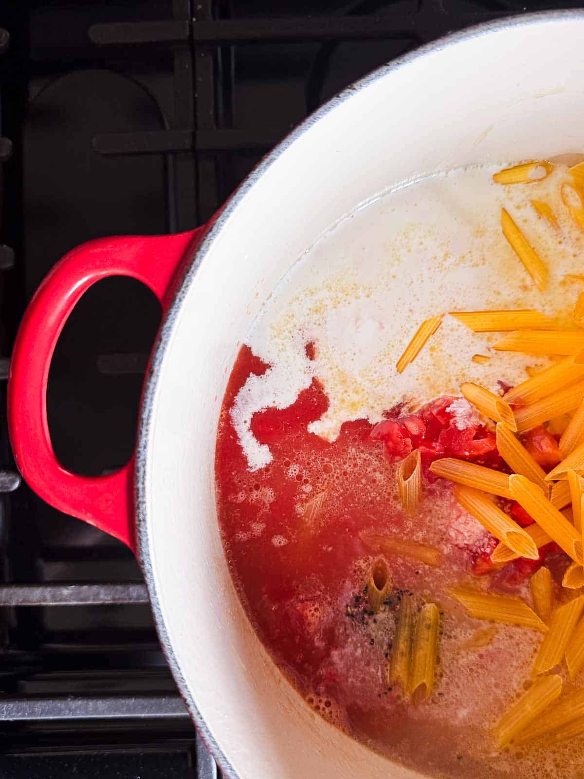 red dutch oven filled with ingredients for to make a pasta recipe on the stovetop.