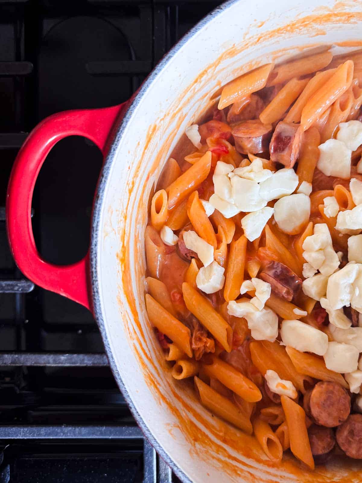red dutch oven with cooked cheesy pasta topped with cheese curds.
