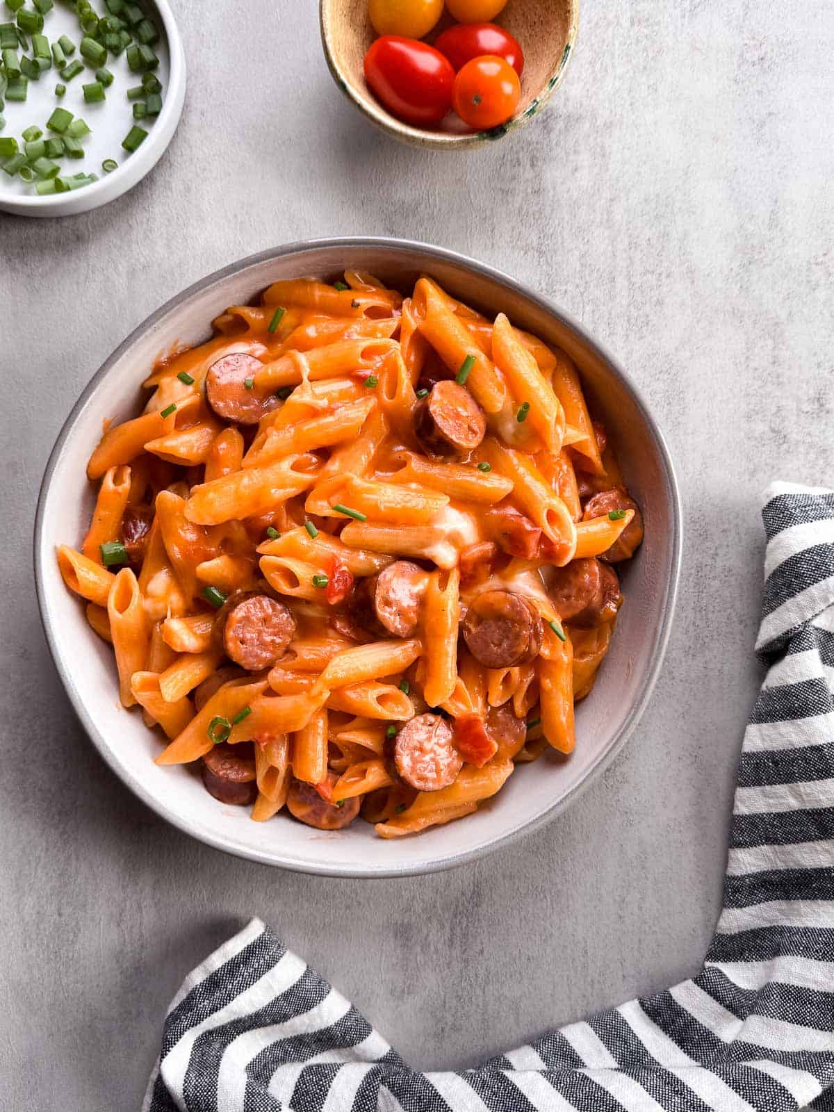 bowl of pasta topped with chopped green onions, alongside cherry tomatoes and chopped green onions.