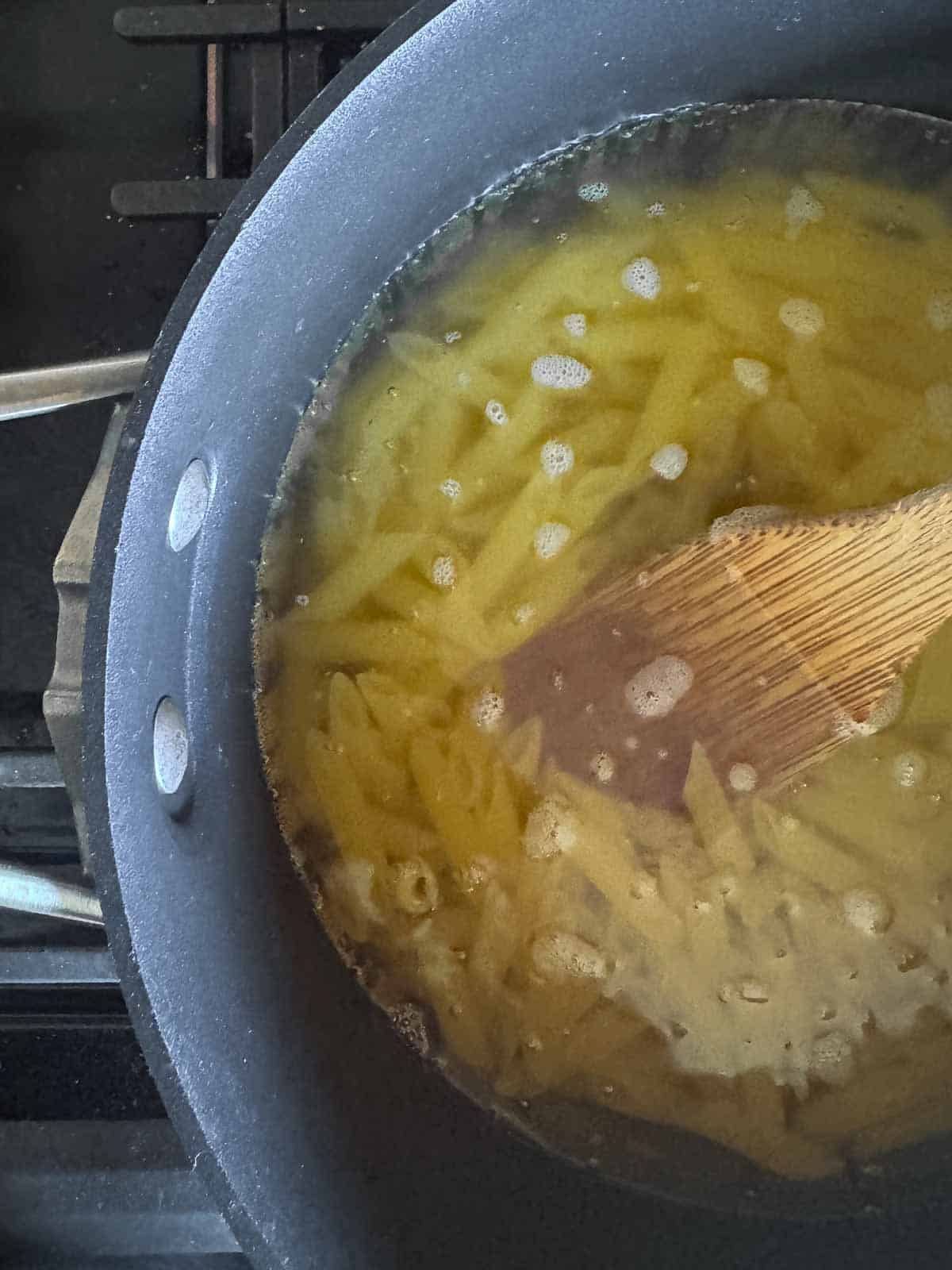 black pot of boiling water with penne noodles inside.