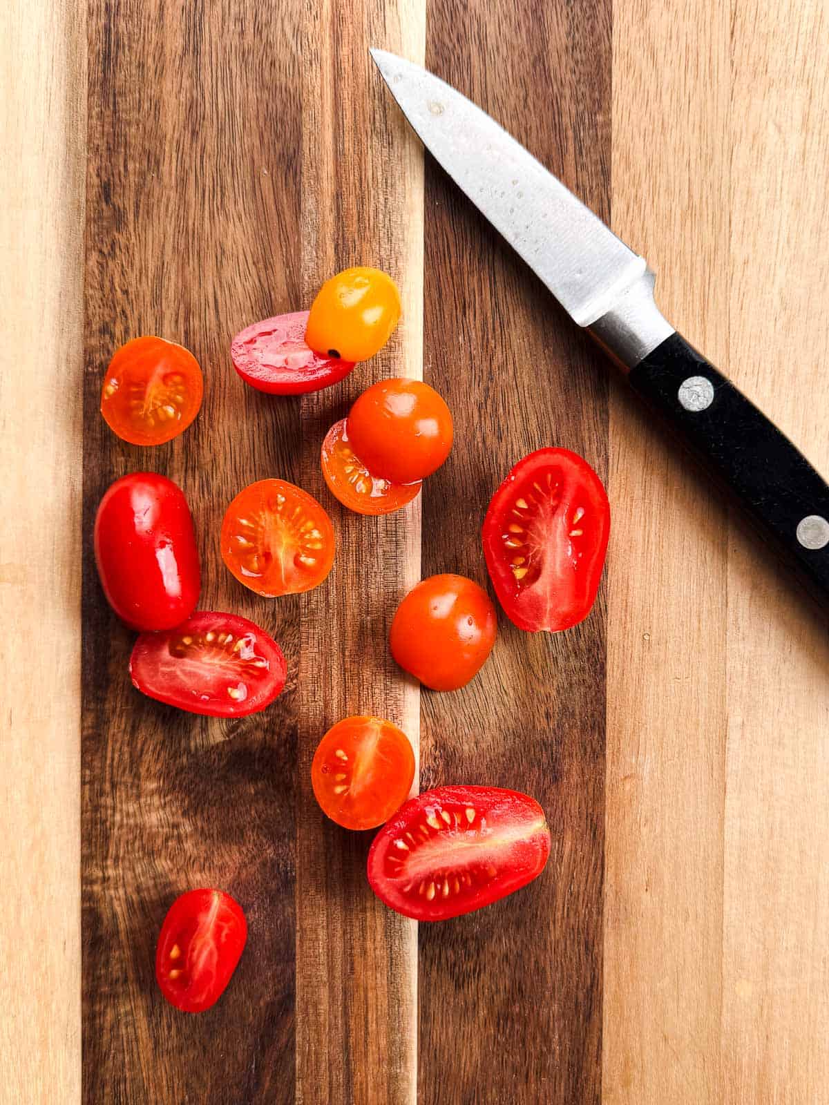 wooden cutting board with halved grape tomatoes and a knife.