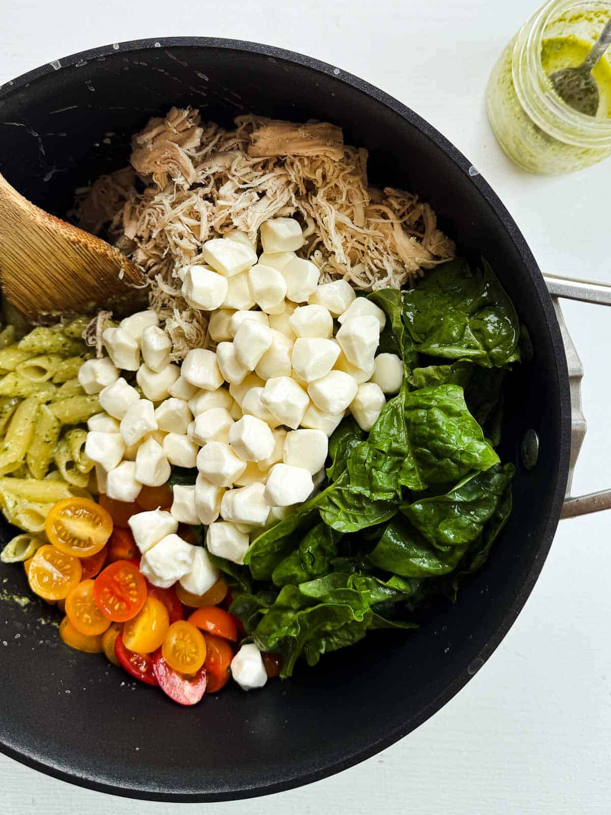 penne noodles covered in sauce with halved tomatoes, spinach, and mozzarella pearls.