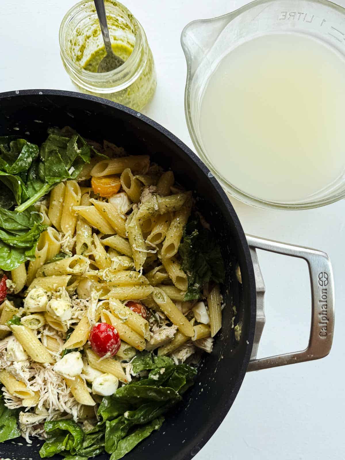 mix pasta ingredients in a black pot next to a bowl of pasta water.
