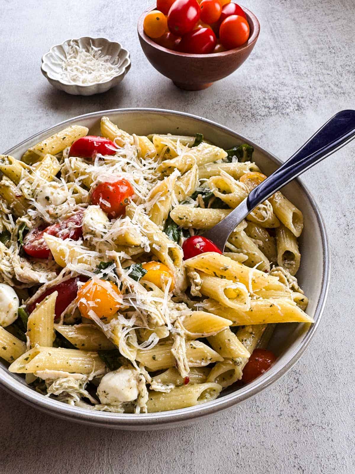 bowl of penne pasta with creamy pesto sauce, spinach and halved tomatoes with a fork.