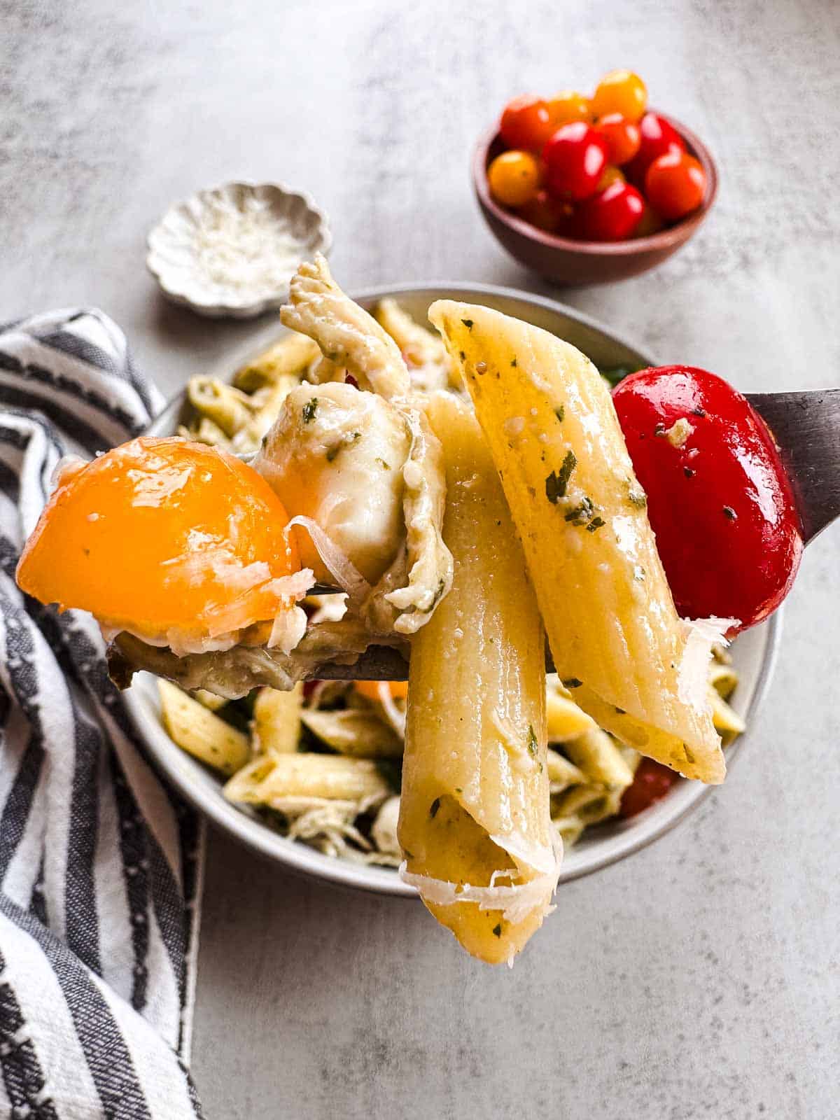 forkful of penne pasta with halved tomatoes, chicken and pesto cream sauce.