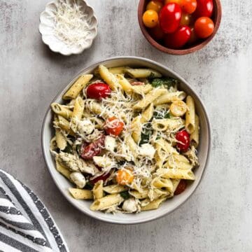 bowl of penne pasta with creamy pesto sauce, chicken, tomatoes, and spinach.