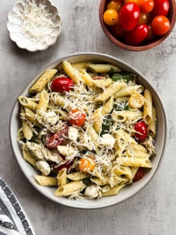 bowl of penne pasta with creamy pesto sauce, chicken, tomatoes, and spinach.