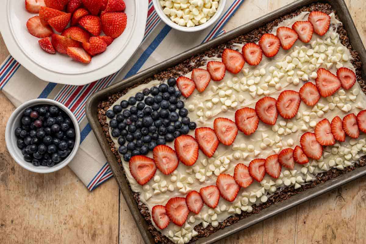 fruit pizza in the shape of a American flag with bowls of berries and white chocolate chips.