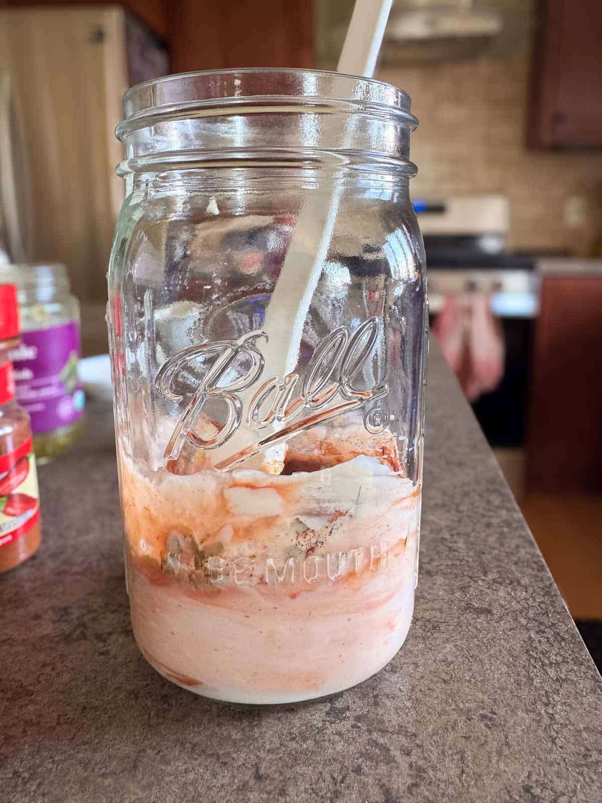 sitting on the countertop a wide mouth mason jar with all the ingredients for thousand island dressing.