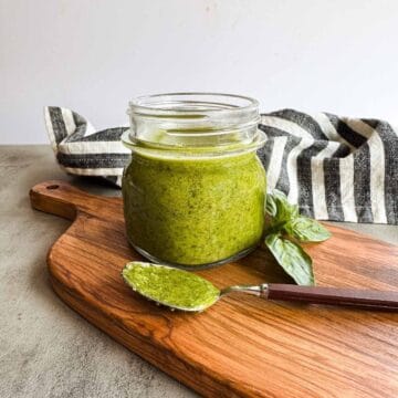 small mason jar full of pesto alongside a spoonful on a wooden board.