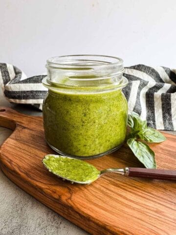 small mason jar full of pesto alongside a spoonful on a wooden board.