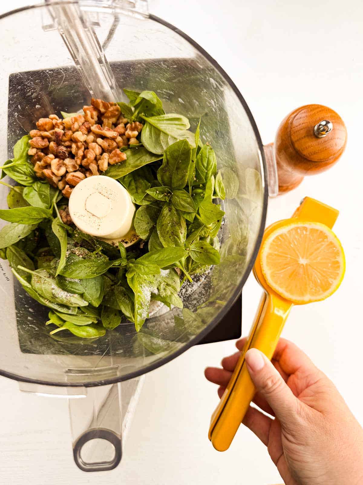 food processor cup with basil, walnuts, salt and pepper alongside a citrus squeezer.